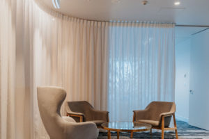 Waiting Area with queen armchair in white and grey armchair. Brass and glass coffee table. White curtain between waiting area and boardroom.