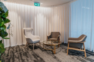 Waiting Area with queen armchair in white and grey armchair. Brass and glass coffee table. White curtain between waiting area and boardroom.