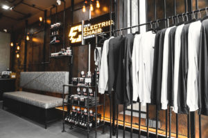 Industrial themed Barber shop waiting area. Rust painted wall with mesh and pipework with feature lighting. Pipework along ceiling and down the wall. Pipework used to create shelving and product display.