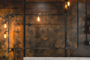 Industrial themed Barber shop waiting area. Rust painted wall with mesh and pipework with feature lighting. Pipework details with integrated lighting fixtures.