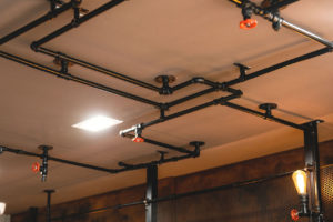 Industrial themed Barber shop waiting area. Rust painted wall with mesh and pipework with feature lighting. Pipework along ceiling and down the wall.