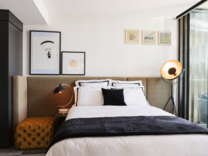 Master bedroom with bespoke headboard, mustard yellow ottoman, standing lamp and wall art.