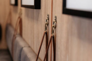 Banquette leather strap detail with wall hook. Suspended banquette padded back on timber wall.